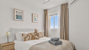 A neatly made bed with a white headboard, a bedside lamp, and a window with curtains. - Luma Riviera, relaxing with sea view and pool. Walking distance to the beach. (Mijas)