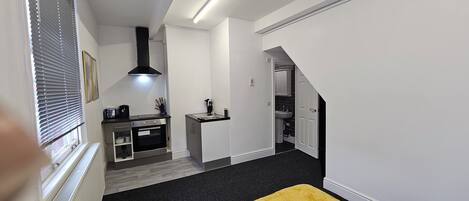 Une chambre d’hôtel de taille réduite comprenant un lit, une kitchenette, une salle de bain et un escalier.