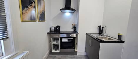 A compact kitchen with a built-in oven, a sink, and a range hood. There are two framed artworks on the wall.