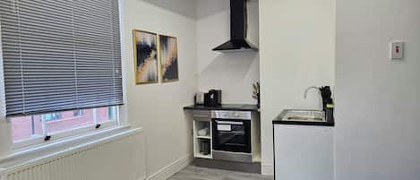 A compact kitchen with a built-in oven, a black range hood, and a small sink.