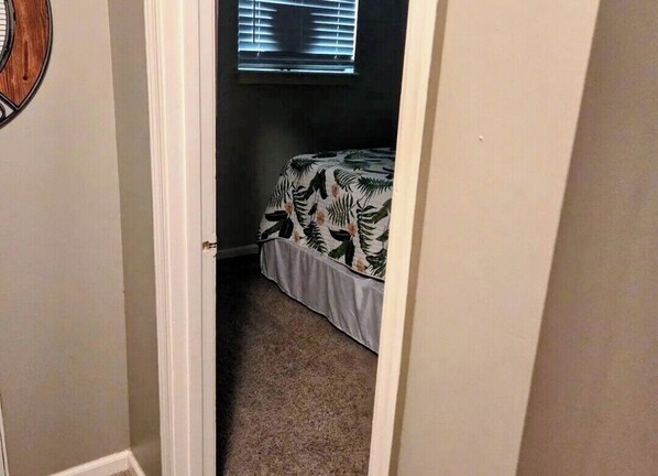 Une chambre à coucher avec un lit, une fenêtre avec des stores et un sol recouvert de moquette.