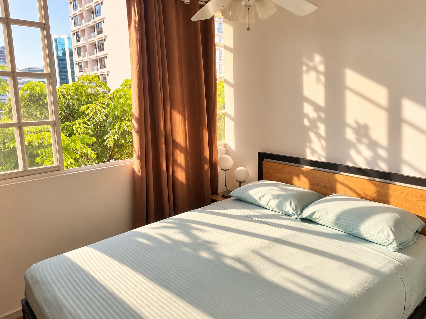 Un lit avec une tête de lit en bois, une fenêtre avec des rideaux et une vue sur la verdure à l’extérieur.