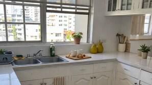 A kitchen with white cabinets, a large window, a sink, and a countertop with a plant and utensils. - Bright & Spacious Apartment in Obarrio | Walk to Everything + City Views (Panamá)