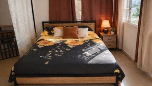 A bed with a floral bedspread, a bedside lamp, and a view of the city through a window. - Bright & Spacious Apartment in Obarrio | Walk to Everything + City Views (Panamá)