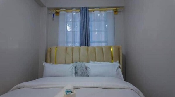 A room with a bed, a window with curtains, and a wall-mounted light fixture.