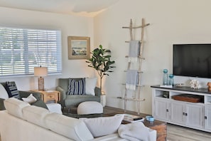 A living room with a sofa, armchair, TV, and a ladder against the wall.