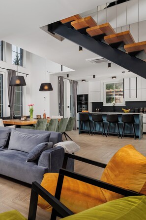 A modern interior with a staircase, dining area, kitchen, and seating.