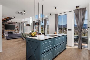 A modern kitchen with a large island, a dining area with a sofa, and a TV mounted on a stone wall.