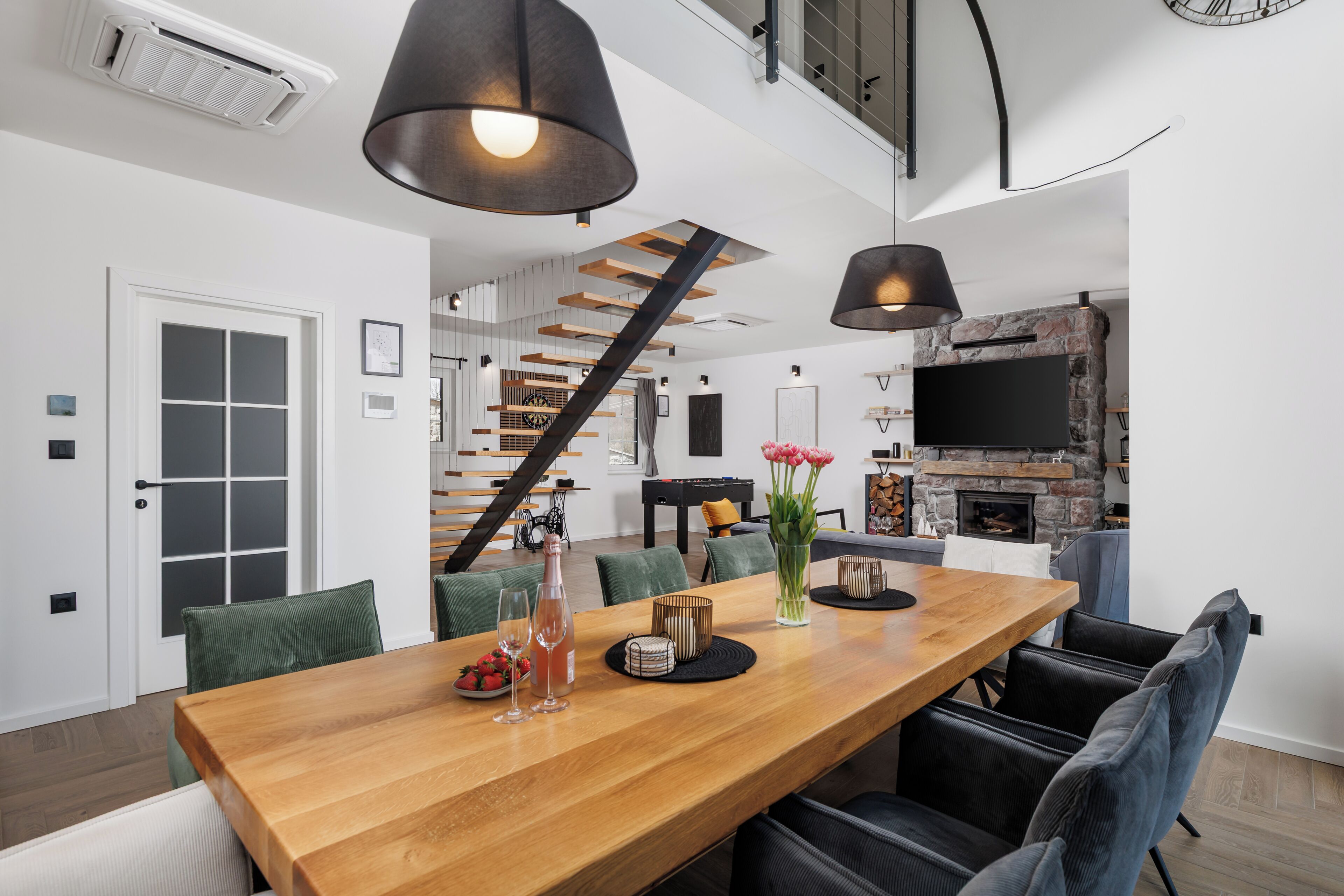 A modern kitchen with a stone fireplace, a dining area with a wooden table and chairs, and a staircase leading to an upper level.