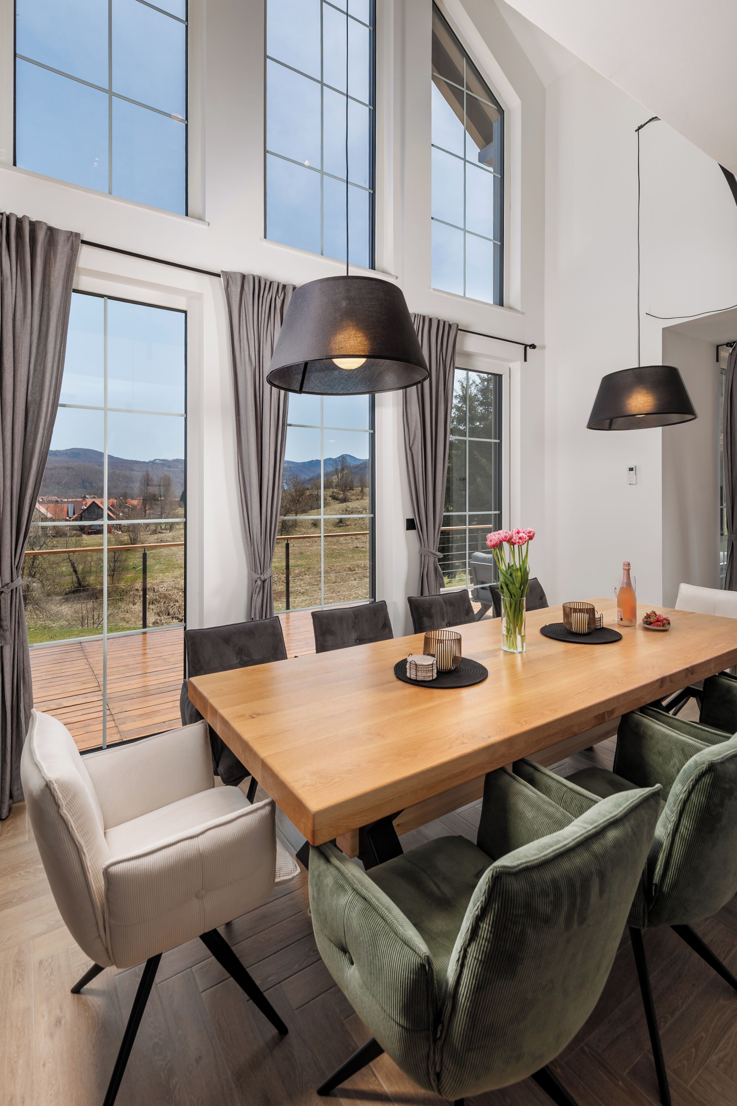Un espace de restauration moderne avec une table en bois, des chaises à revêtement vert et de grandes fenêtres donnant sur la campagne.
