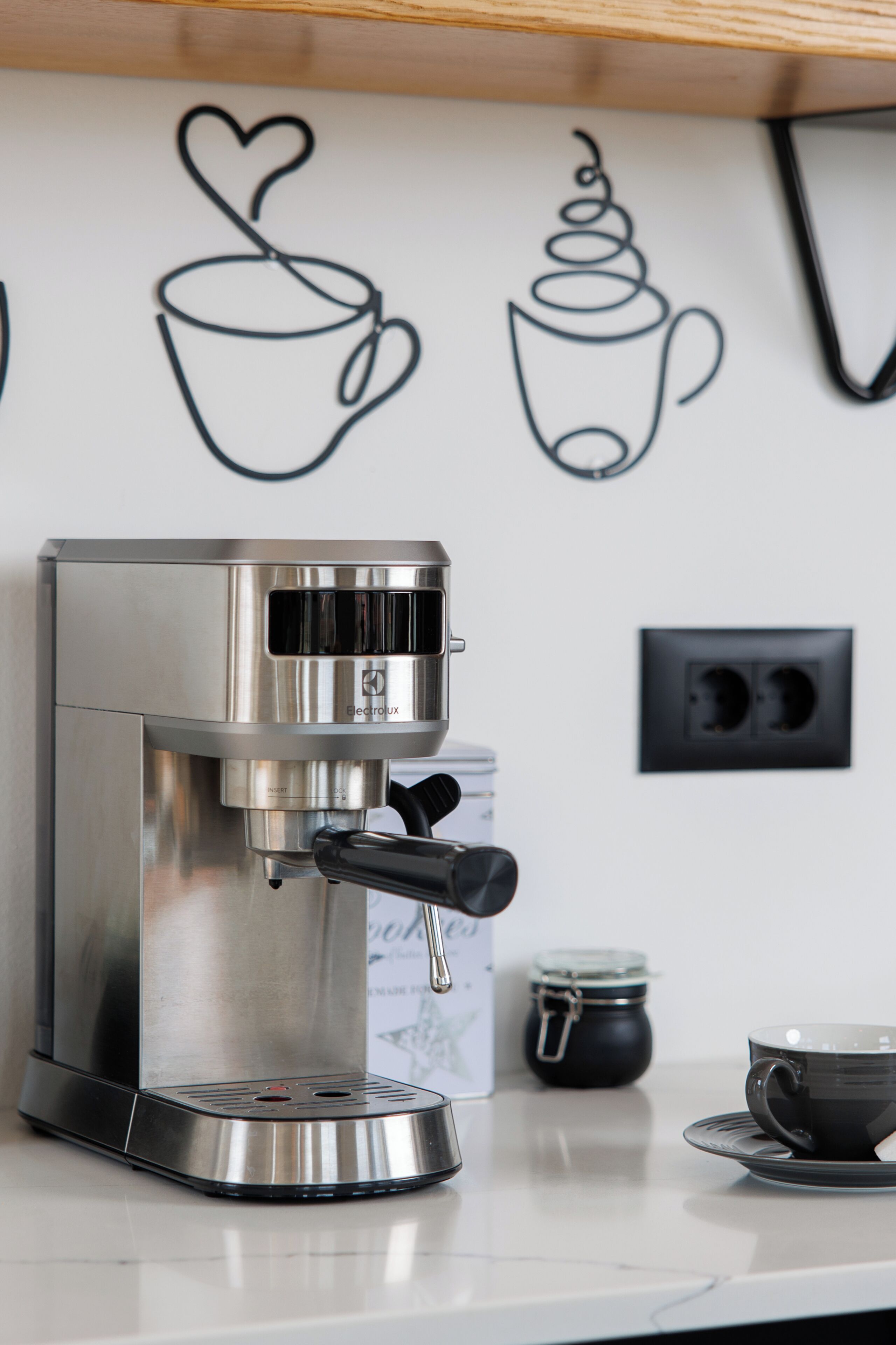 A coffee machine on a kitchen counter with a wall decoration of a cup and heart.