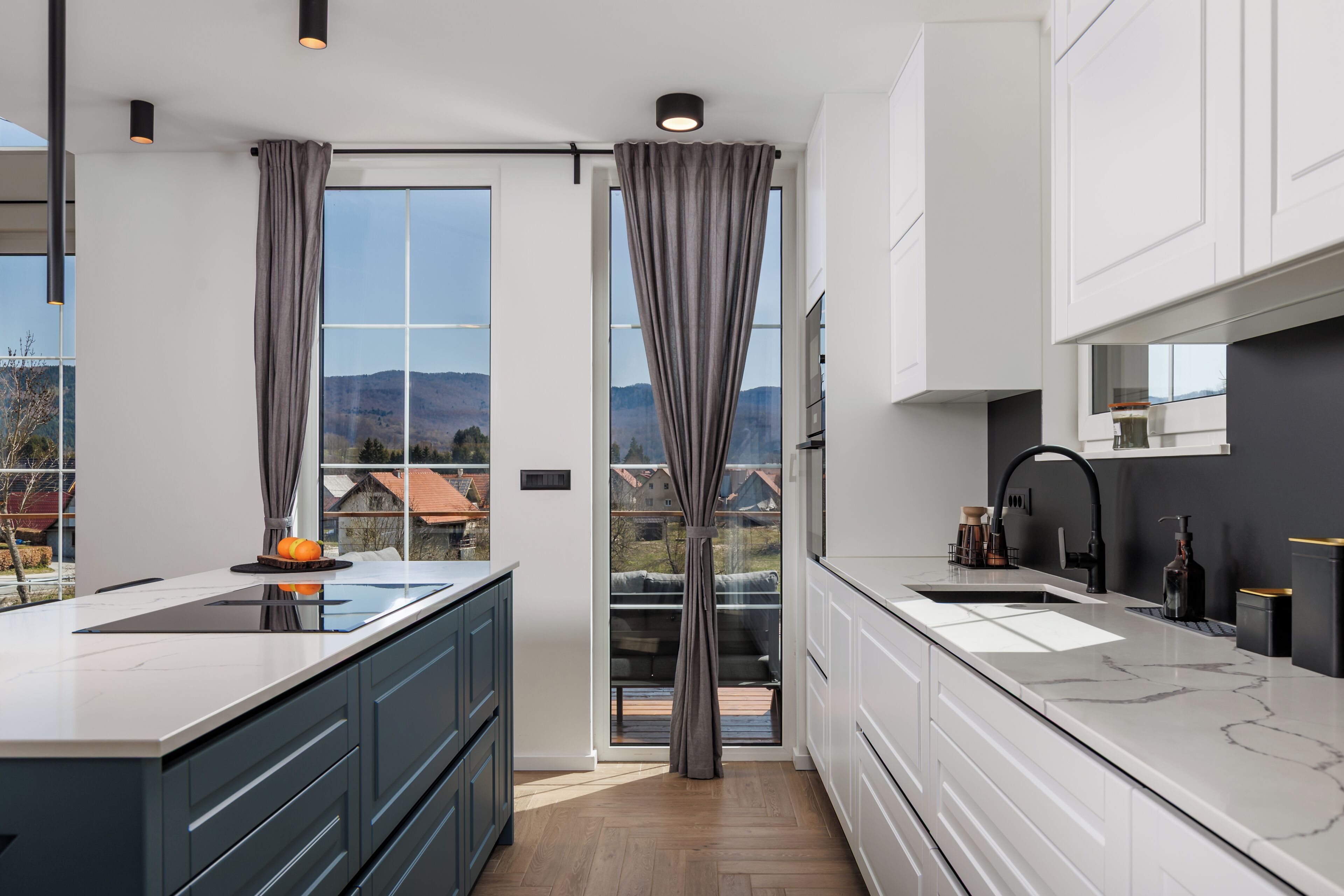 A modern kitchen with a large island, a double sink, and a view of the mountains through the windows.