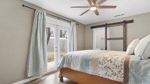 Ein Schlafzimmer mit einem Bett, einem Deckenventilator, einem Fenster mit Vorhängen und Blick ins Freie.
