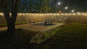 Ein Terrassenbereich im Freien mit Holzzaun, Lichterketten und Gartenmöbeln.