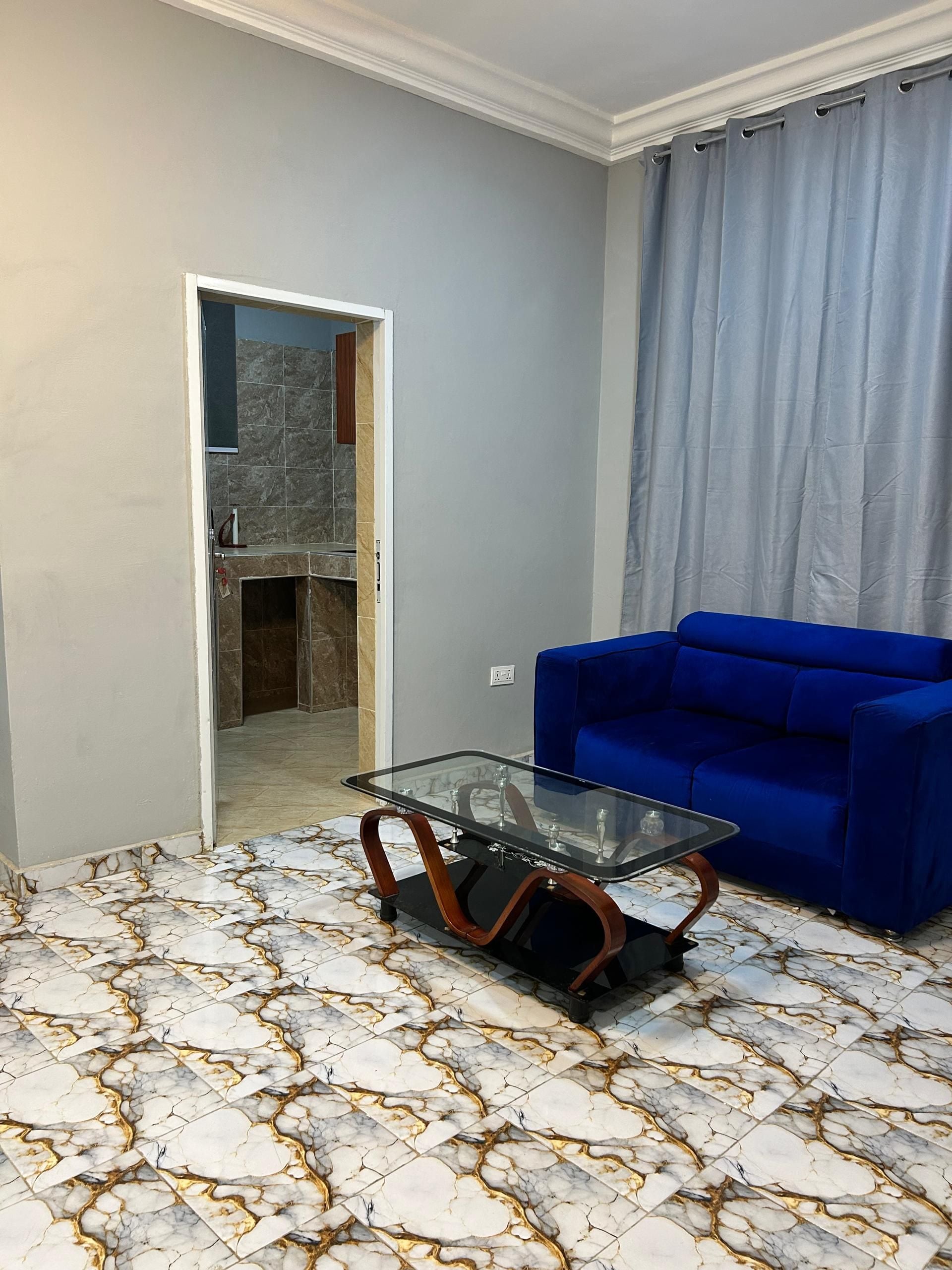 Een kamer met een tafel met glazen blad, een blauwe bank en een vloer met patroon.
