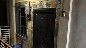 Un couloir avec un sol à motifs, une porte noire et une chaise bleue.