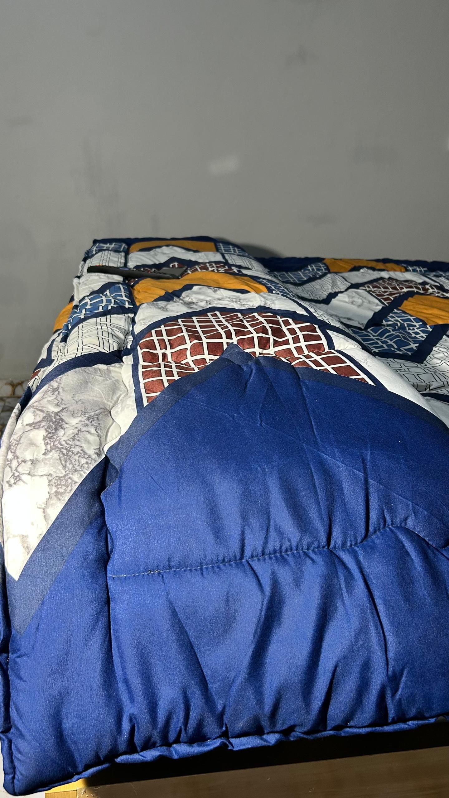 Egy ágy, mintás ágytakaróval és egy kék párnával.