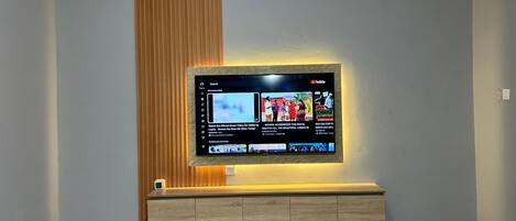 A flat-screen TV mounted on a wall with a wooden panel and a marble-patterned floor.