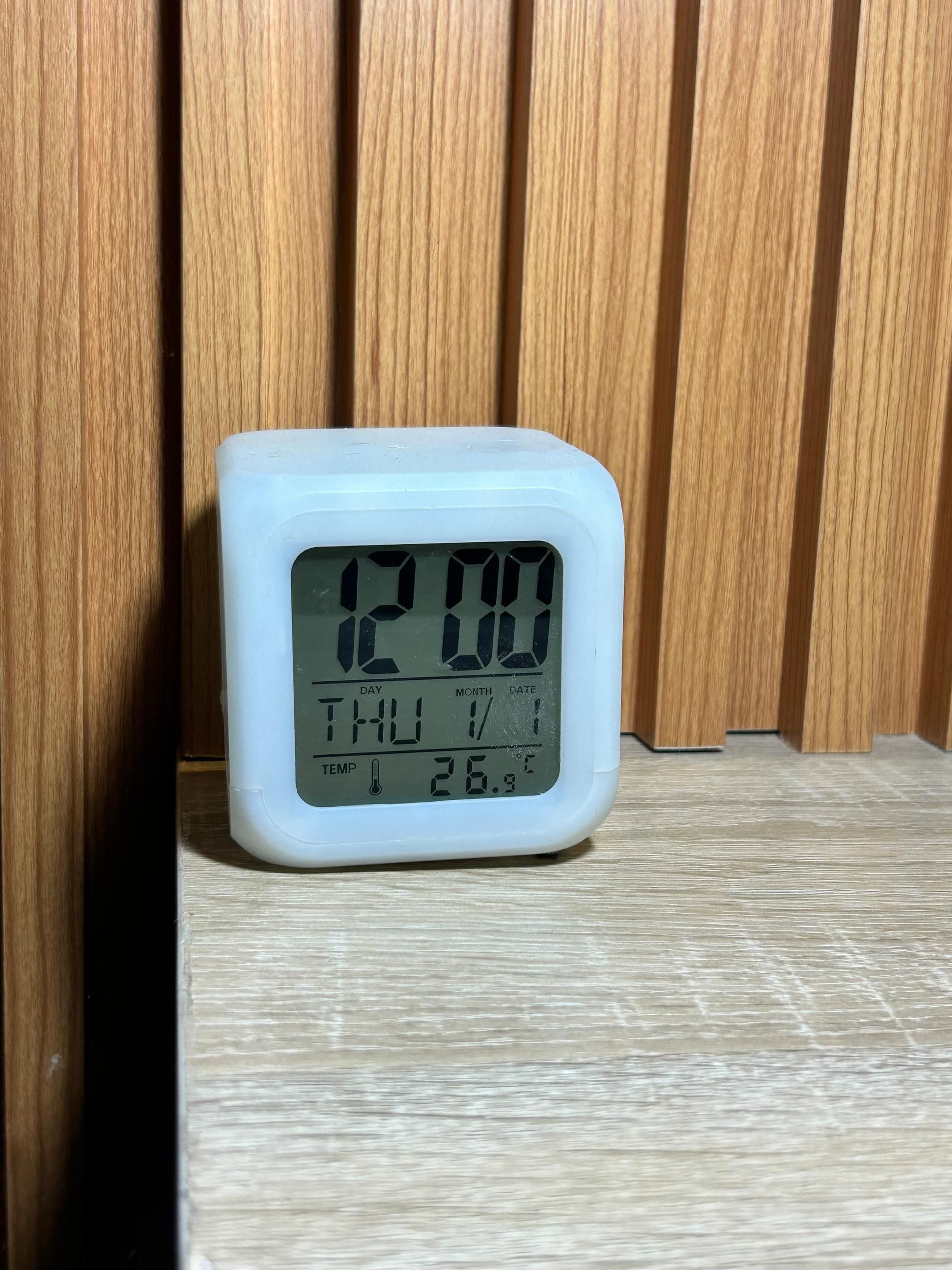 Un reloj digital muestra la hora: 12:00, día jueves, con una temperatura de -3.4 grados Celsius.