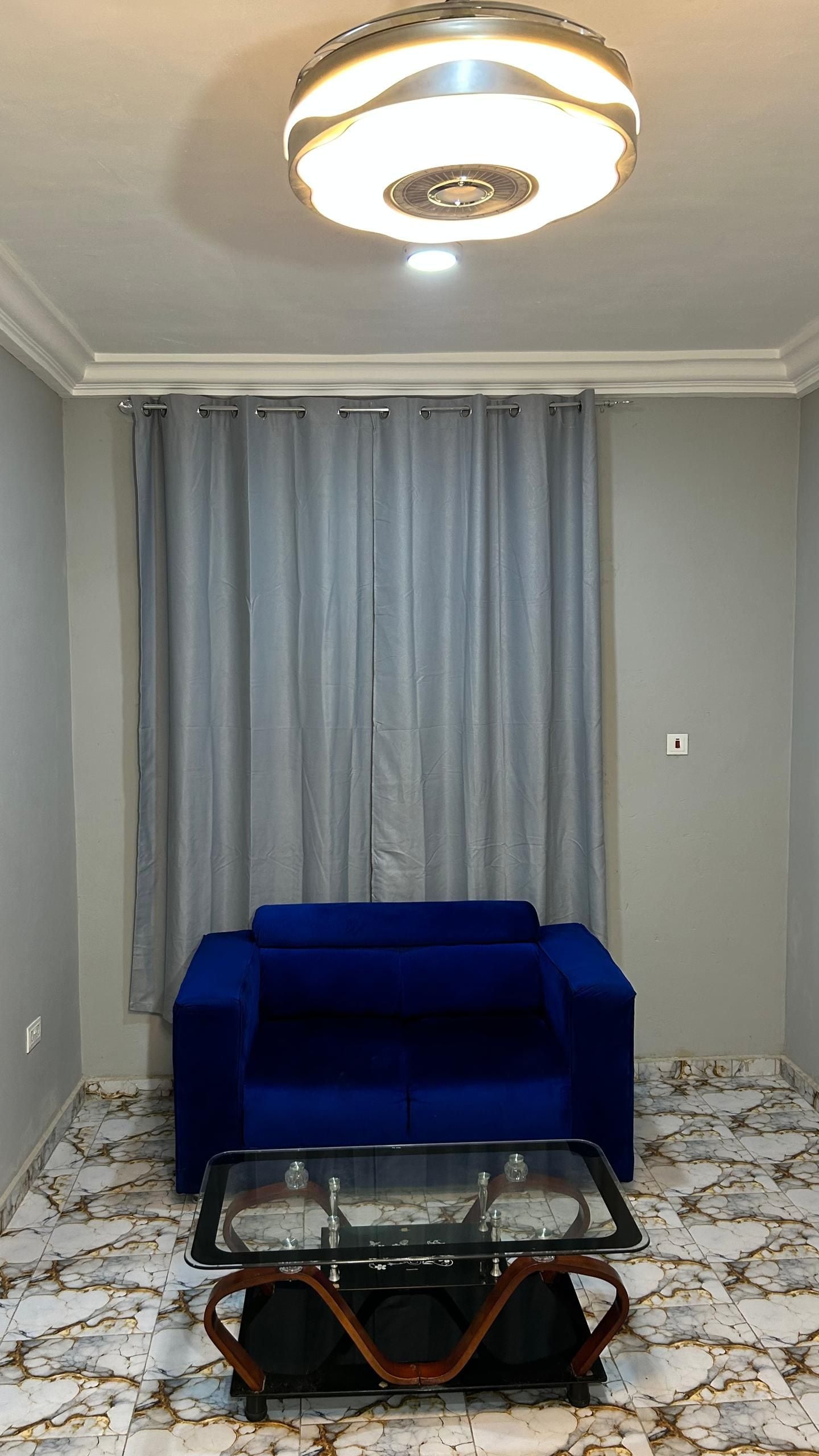 A living room with a blue sofa, a glass coffee table, and a patterned floor.
