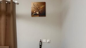 Une pièce avec un lit, un canapé bleu, un tableau et un thermostat fixé au mur.