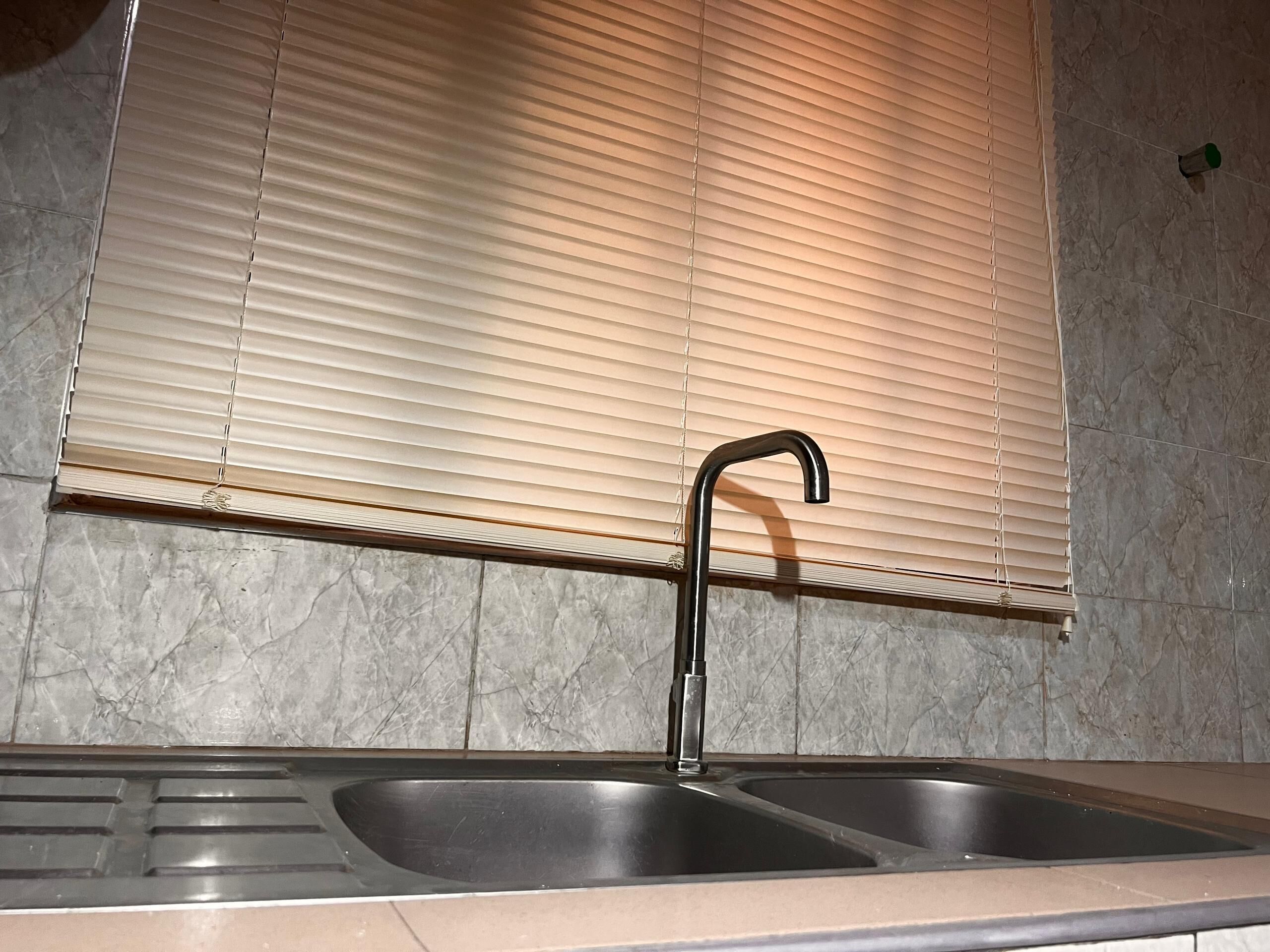 Una cocina con un lavamanos doble, un grifo y una ventana con persianas.