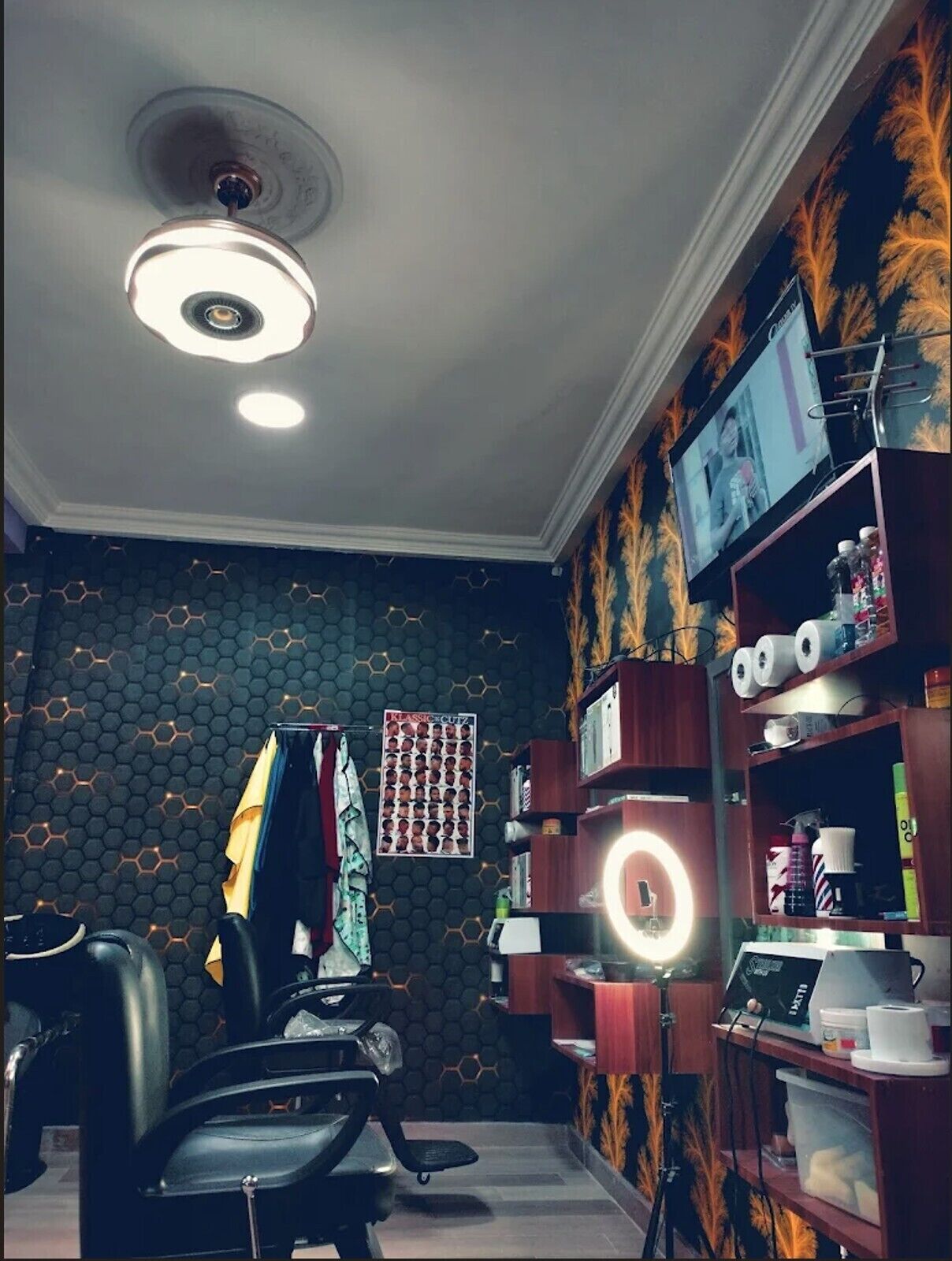 Une pièce avec un mur orné d’un motif hexagonal, un luminaire au plafond, une chaise, un bureau avec un ordinateur et une étagère contenant divers objets.