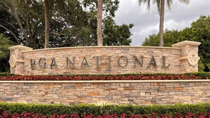 A stone wall with 'PGA NATIONAL' signage, surrounded by well-maintained grass and red foliage. - 2 BEDROOM VILLA IN PARADISE...PGA NATIONAL...BEST PLACE TO BE! (Palm Beach Gardens)