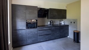 A modern kitchen with dark cabinetry, a built-in oven, a coffee maker, and a kettle.