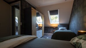 A bedroom with two beds, a wardrobe, a skylight, and a small table with a lamp.