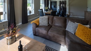 A living room with a brown sofa, a wooden coffee table, and a vase with dried flowers.