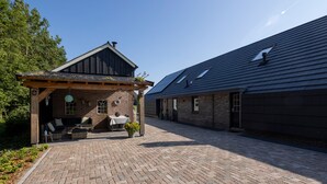 A building with a brick facade, a wooden porch with seating, and a paved courtyard.