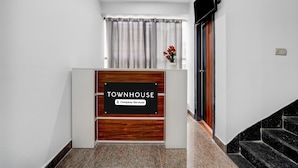 Un mostrador de recepción con un letrero que dice 'TOWNHOUSE Company Serviced', una ventana con cortinas y una escalera a la derecha.