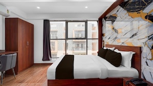 Habitación de hotel con una cama grande, un escritorio, un armario y vista a la ciudad desde la ventana.