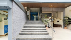 Una escalera conduce a una entrada con portón, barandilla metálica, una planta en maceta y una puerta azul al fondo.