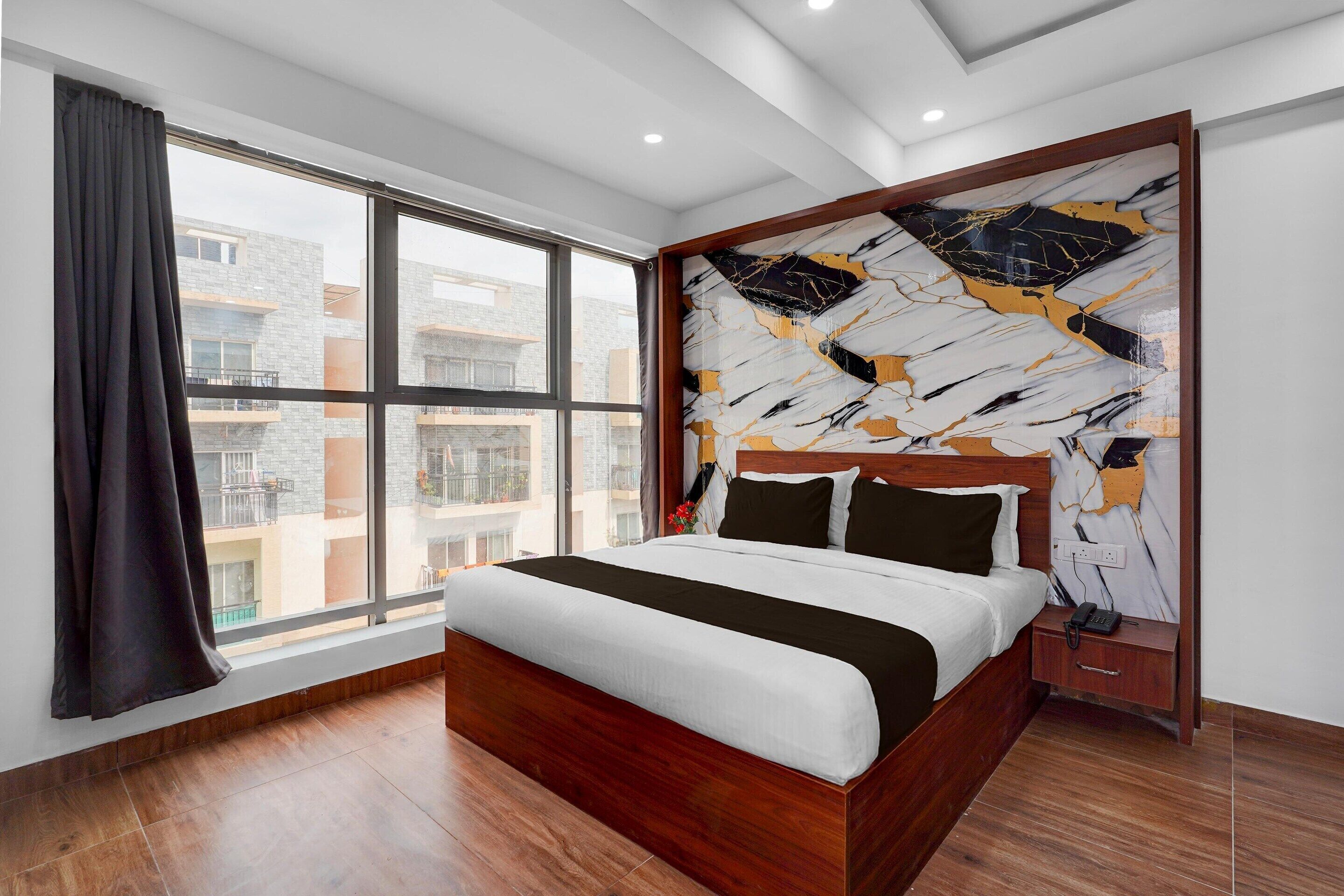 A modern hotel room with a large bed, a view through a window, and a marble-patterned wall.