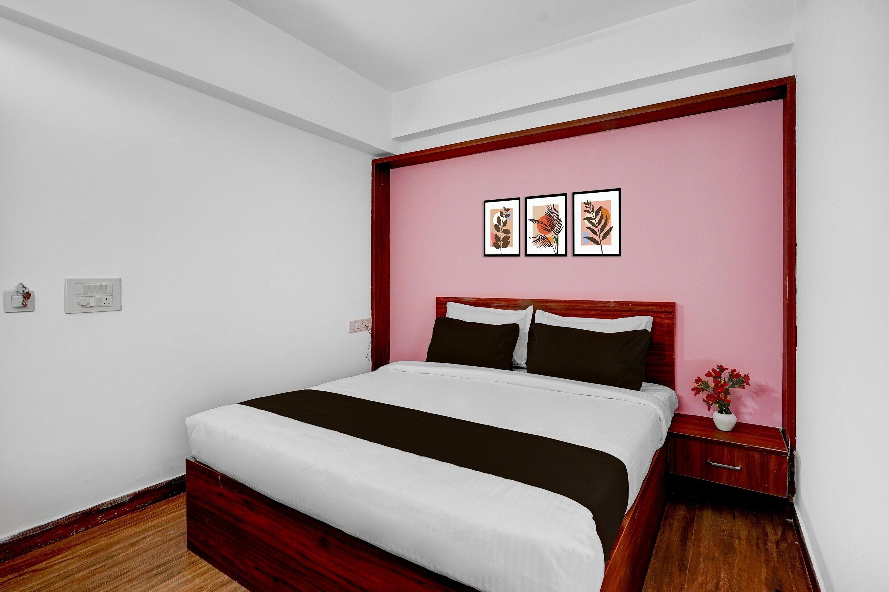 A bedroom with a bed, a nightstand, a wall-mounted power outlet, and a wall with three framed pictures.