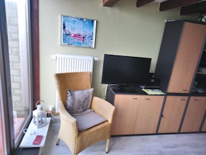 Ein Zimmer mit einem Korbsessel, einem Fernseher, einem Schrank und einem Fenster.