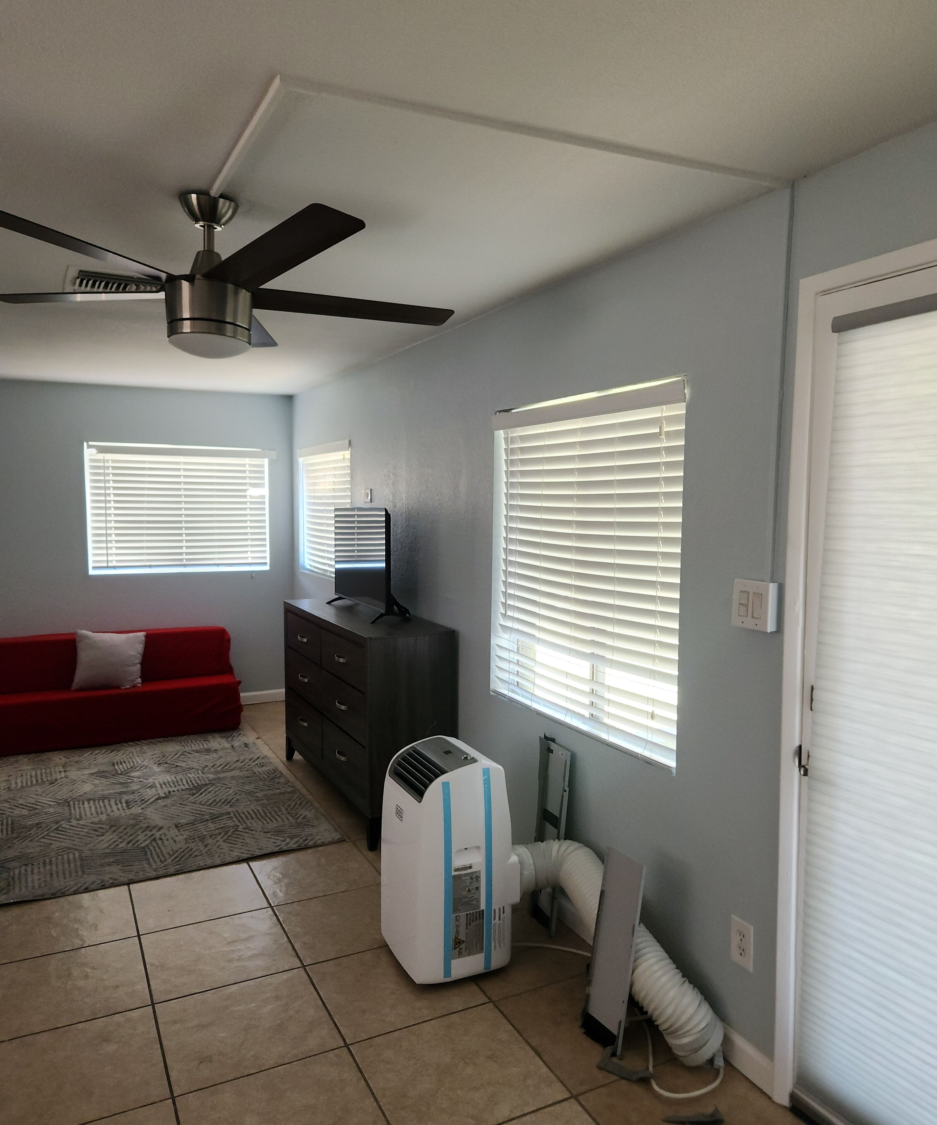 A living room with a ceiling fan, a red couch, a black dresser, and a white air conditioning unit.