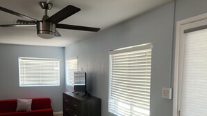 Un salon avec un ventilateur de plafond, un canapé rouge, une commode noire et un appareil de climatisation blanc.