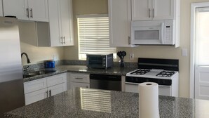 Une cuisine avec des meubles blancs, un four à micro-ondes, un grille-pain, une cuisinière à gaz et un rouleau d’essuie-tout.