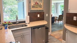 A modern kitchen with a built-in dishwasher, a window with blinds, and a framed painting on the wall. - Mountain House in Town (Falls Church)