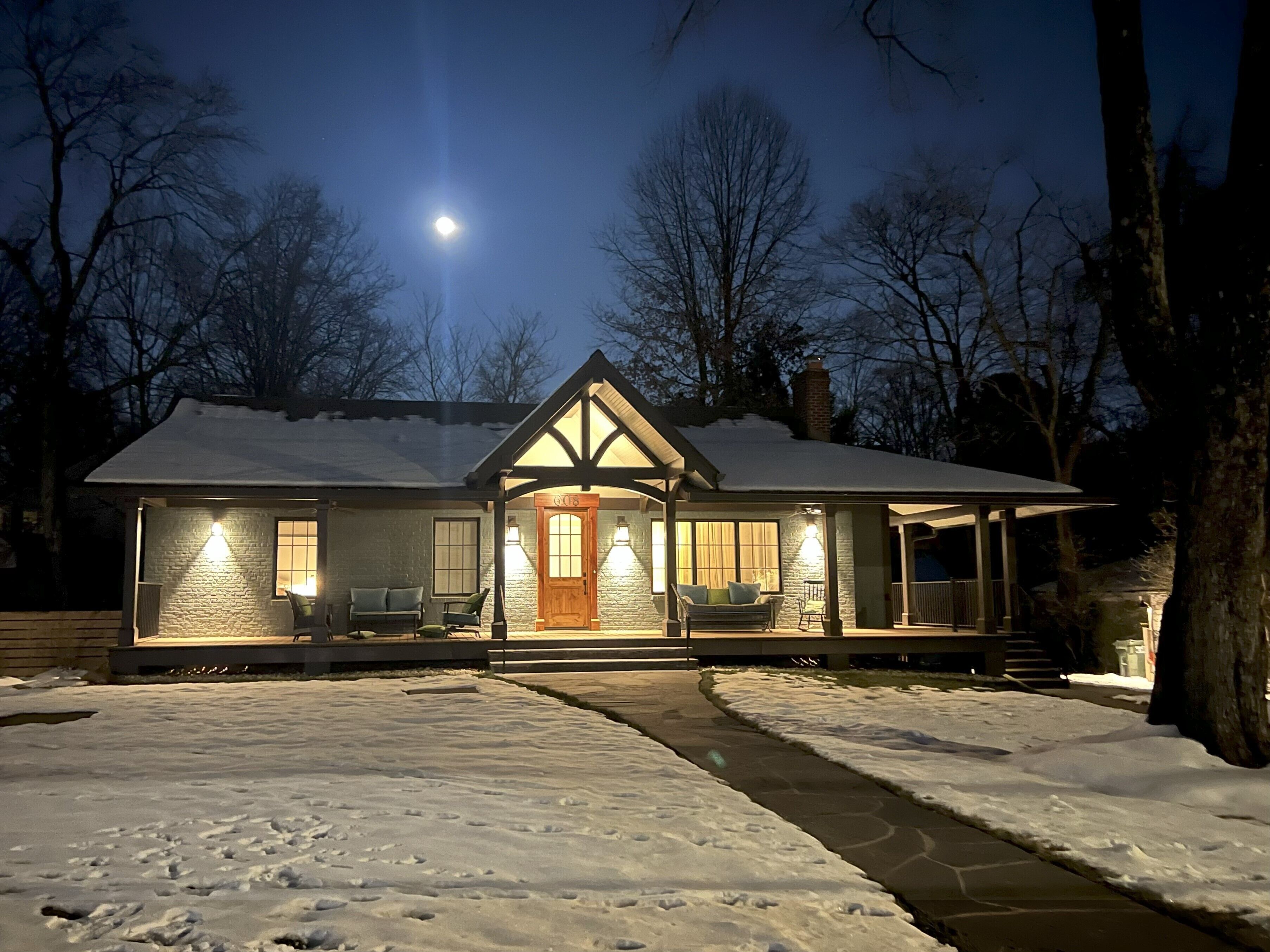 A snow-covered house with a front porch, a chimney, and a moon in the sky.