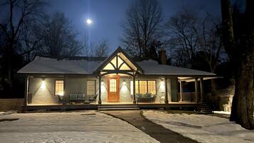 A snow-covered house with a front porch, a chimney, and a moon in the sky.