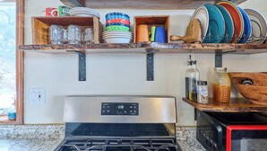 Una cocina con estufa de acero inoxidable, microondas y repisas de madera con vajilla y frascos.