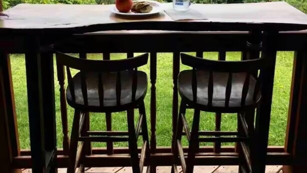 Una mesa con dos sillas, un plato de comida y una taza, con vistas a un paisaje boscoso.