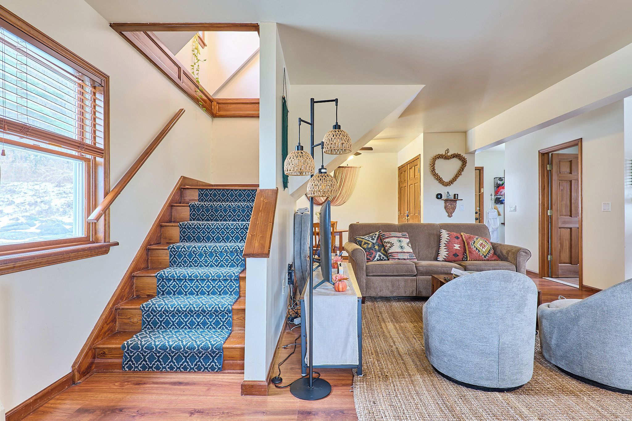 Eine Treppe mit gemustertem Teppich, ein Wohnzimmer mit einer Couch und Kissen, ein runder Hocker und eine Pendelleuchte.