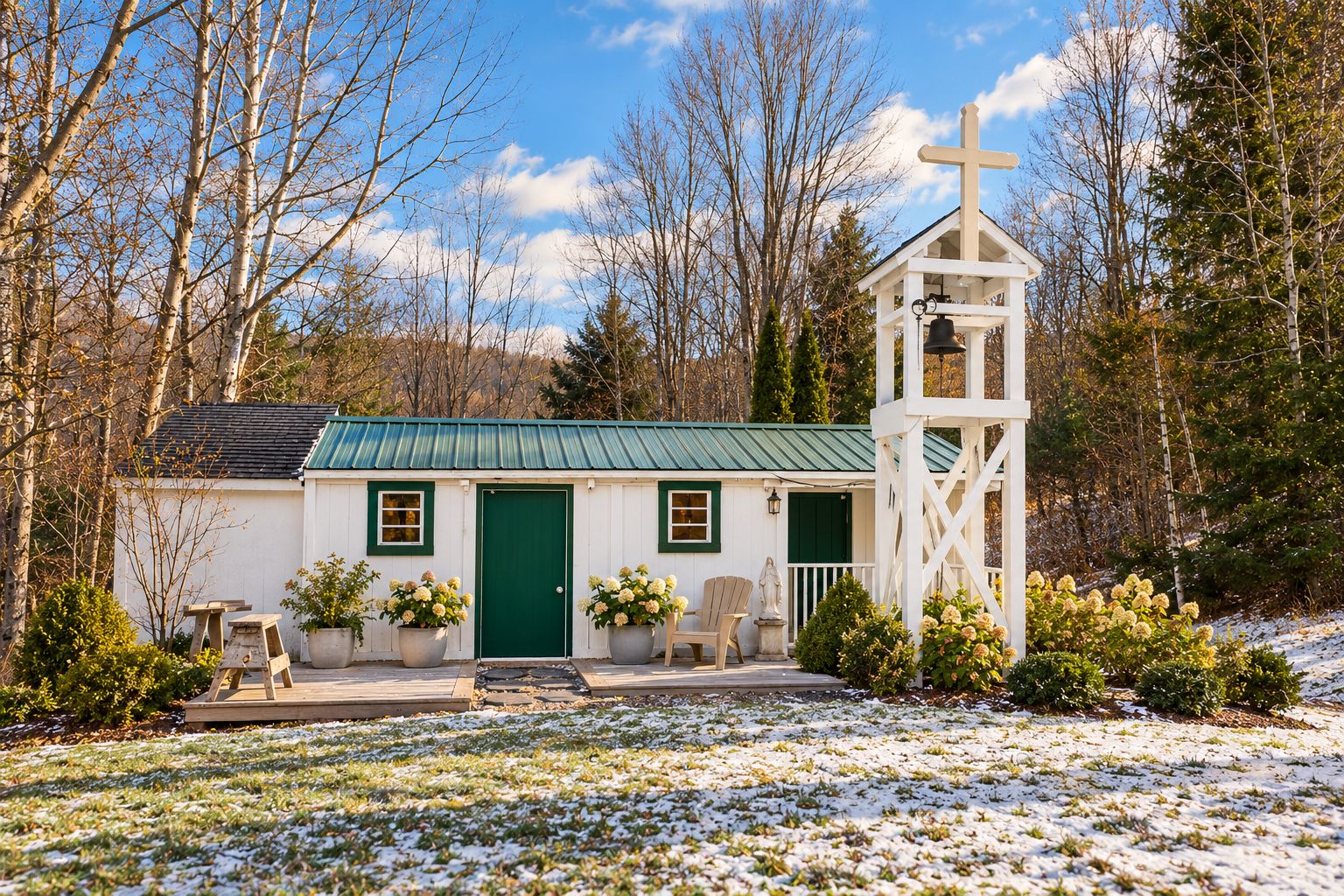 A small white church with a green door and a bell tower, surrounded by trees and snow.