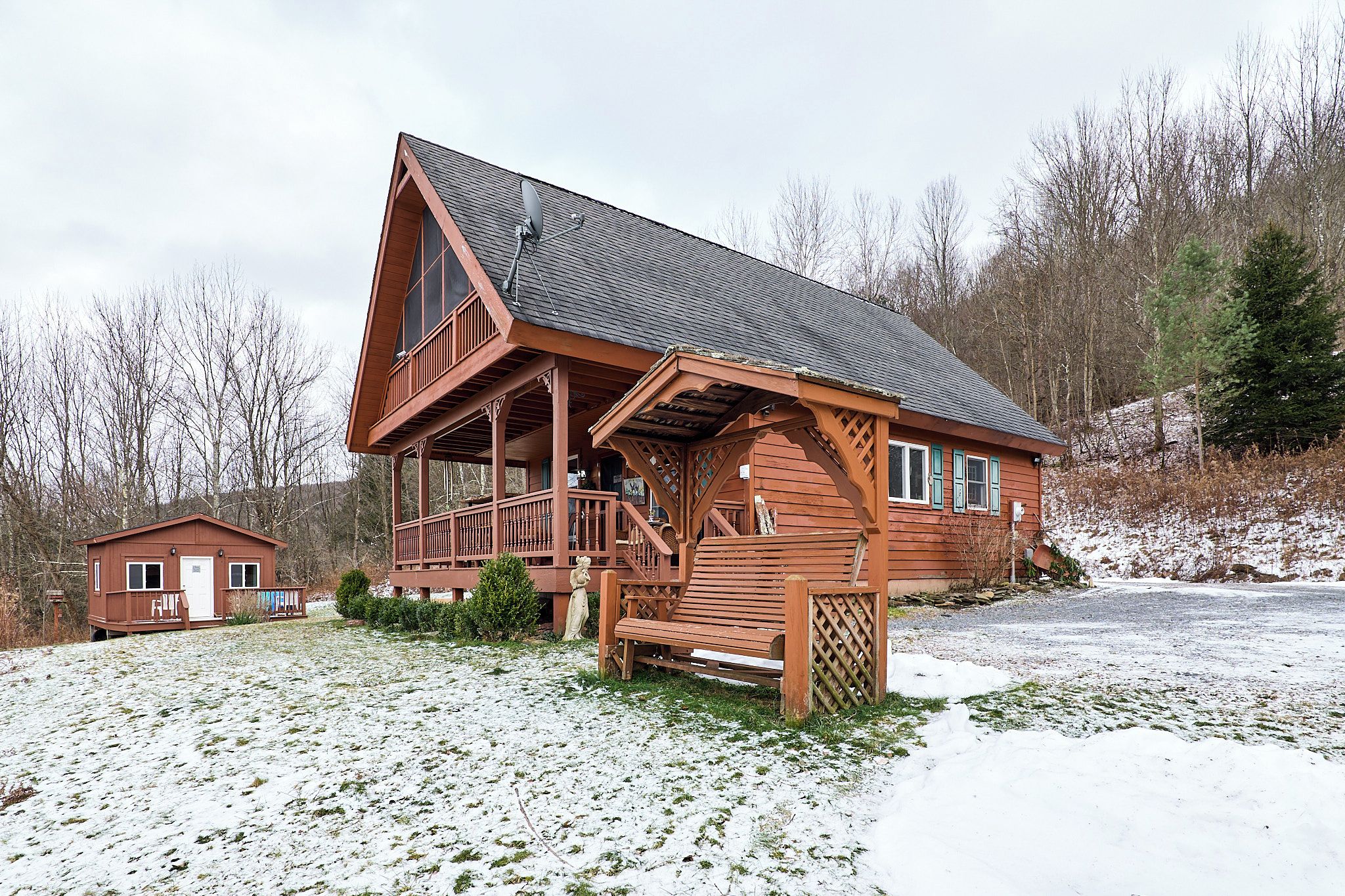 Eine Holzhütte mit einem Balkon, ein kleines Nebengebäude und eine verschneite Landschaft.