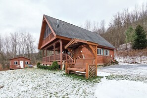 Una cabaña de madera con balcón, un edificio pequeño adyacente y un paisaje nevado.